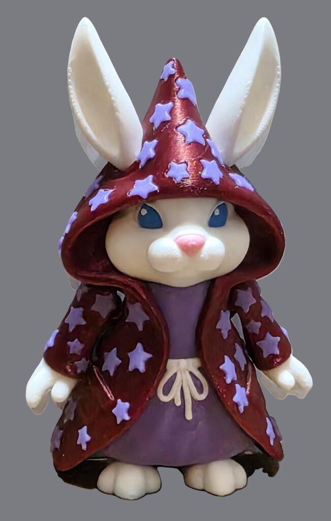 Photo of 3D printed white flexi wizard bunny in purple robe with blue starts